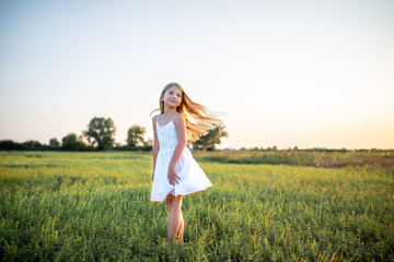 Fototapeta na wymiar adorable little child in white dress posing on field on sunset