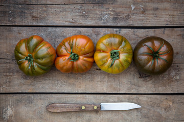 Reife farbige Tomaten zusammen mit einem Messer auf einem alten Holzuntergrund