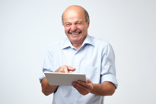 Euphoric winner mature caucasian man laughing with a tablet. He saw very funny video or joke.