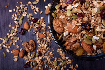 Granola made of cereals, nuts and seeds in a bowl and scattered around the dark table