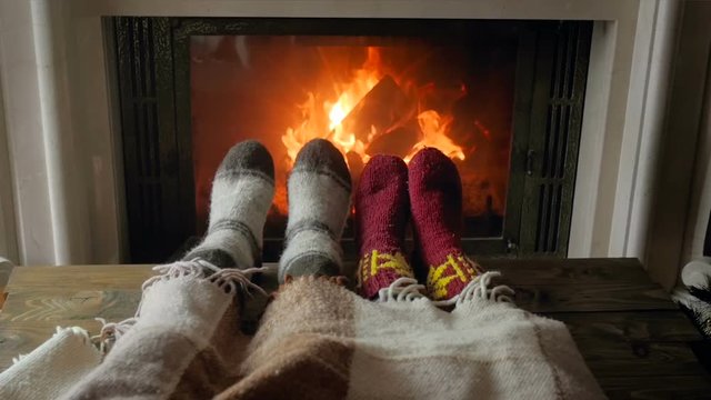 Slow motion video of roamntic couple lying under blanket and warming feet by burning fireplace at night