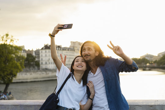 France, Paris, happy young couple taking a selfie at river Seine at sunset