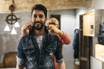 Handsome man trying on new denim jacket with stylist in modern boutique