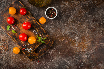 Red and yellow cherry tomatoes, a bottle of olive oil, salt, pepper and basil