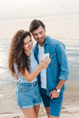 young smiling couple using smartphone near sea