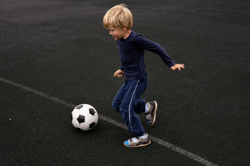 active lifestyle in a modern city - little boy playing with a soccer ball at the stadium