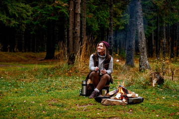Wanderlust and Travel concept. Woman roast marshmallow candies on the campfire in forest. Spring or autumn camping