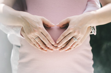 Heart shaped hands over a belly of pregnancy, hand of a man and a women