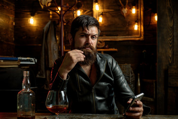 Fototapeta na wymiar Bearded man wearing suit and drinking whiskey brandy or cognac. Sommelier tastes alcohol drink. Degustation and tasting. Portrait of young man holding glass of cognac whiskeyand brandy. Elegant man