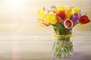 Bunch of Colorful tulip flowers in glass vase on wooden table background with space for text