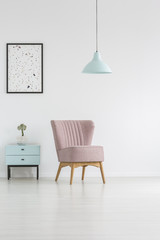Lamp above pink chairs next to blue cabinet with plant in white flat interior with poster. Real photo