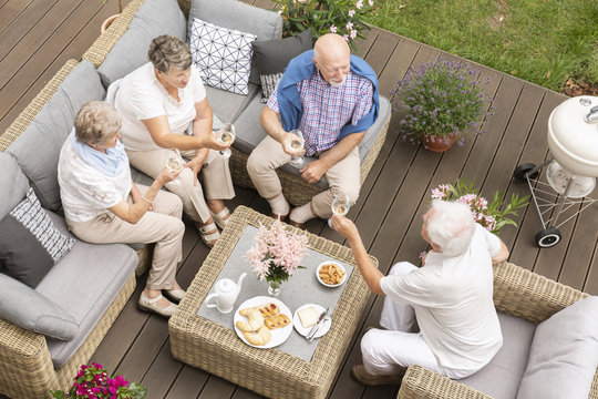 Top view of old friends reunion outside on a wooden deck. Happy seniors making a toast during their celebration.