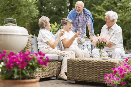 Two senior couples having a social gathering outside on a patio in the garden on summer afternoon. Making a toast.