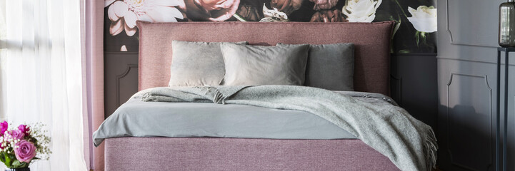 Real photo of dirty pink double bed with grey sheets standing in dark bedroom interior with window...