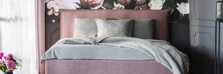 Real photo of dirty pink double bed with grey sheets standing in dark bedroom interior with window with curtains