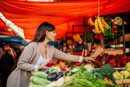 Cheerful woman buying fresh vegetables farmers market.