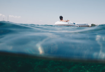Naklejka premium half underwater view of a young boy on rubber dinghy floating on the sea of Sardinia - Italy