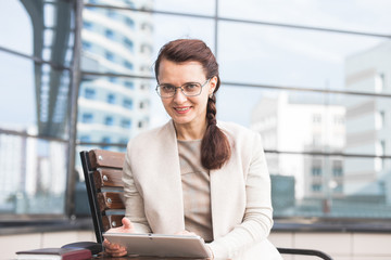 business lady in a suit is sitting at a table with digital tablet against a background of glass buildings