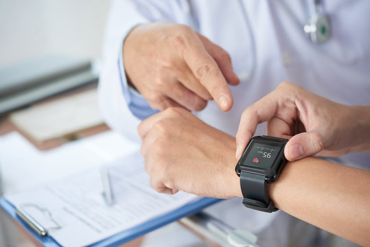 Hands of anonymous patient using fitness tracker to show medical practitioner hear rate during checkup in doctor's office