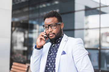 black man businessman in a business suit, expensive watch and glasses sitting on a bench against the backdrop of a modern city