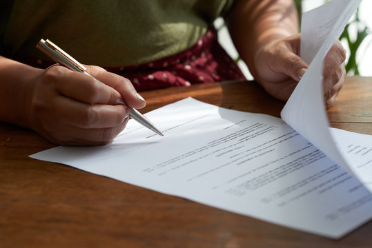 Anonymous lady sitting at table in cafe and signing important documents with pen
