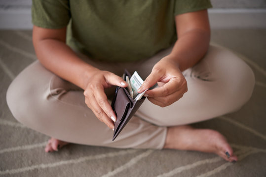 Anonymous lady sitting on floor and checking money inside stylish purse