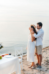 young man closing eyes and making surprise for girlfriend, romantic date on beach