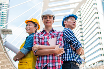 Three Industrial engineer wear safety helmet engineering standing with arms crossed on building outside. Engineering tools and construction concept.
