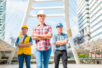 Three industrial engineer wear safety helmet standing on building outside. Engineering tools and construction concept. With copy space for your text.