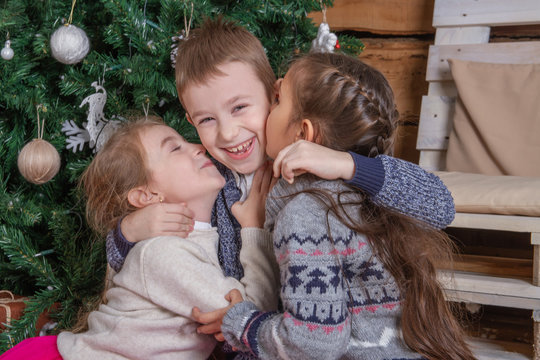Teen girls kissing brother under Christmas tree, everybody laughing