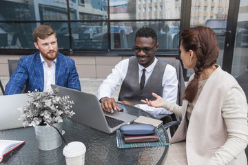 Group of happy diverse male and female business people team in formal gathered around laptop computer in bright office against the background of a glass building
