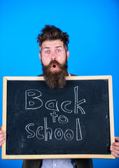 Teacher bearded man stands and holds blackboard with inscription back to school blue background. Continue your education with us. Teacher invites to continue studying. New semester in school