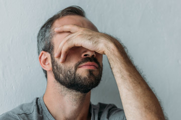 close-up view of bearded frustrated mid adult man with hand on face
