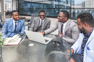 Group of happy diverse male and female business people team in formal gathered around laptop computer in bright office against the background of a glass building