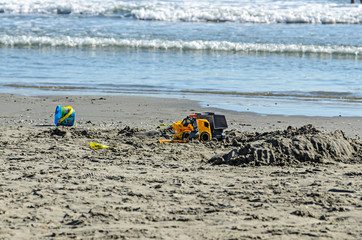 Fototapeta na wymiar Blue toy bucket and truck in the sea sand near blue water and beach, Black Sea shore