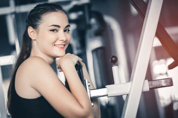 Fit beautiful young woman exercise workout on machine in gym. Glad smiling girl is enjoy with her training process. Concept of fitness, Healthy, Sport, Lifestyle