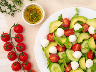 Fresh salad. Tomatoes, cucumbers, arugula, mozzarella, avocado. Fragrant oil with rosemary thyme, top view