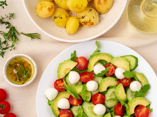 Fresh salad. Tomatoes, cucumbers, arugula, mozzarella, avocado. Fragrant oil with rosemary thyme, baked potato, top view