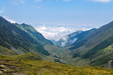 Obraz premium The Transfagarasan road in Fagaras mountains, Carpathians with green grass and rocks, peaks in the clouds