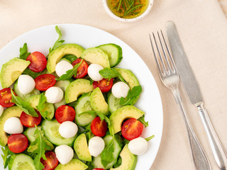 Fresh salad. Tomatoes, cucumbers, arugula, mozzarella, avocado. Fragrant oil with rosemary thyme, top view, close up