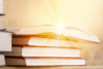 Pile of books with open book with rays of light. The concept of knowledge and enlightenment. Bookshelf with piled books.