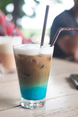A multicolored, three layered opaque coffee in a glass with ice