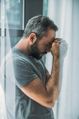 side view of depressed frustrated bearded man standing near window