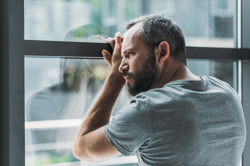 upset bearded man leaning at window and looking through it