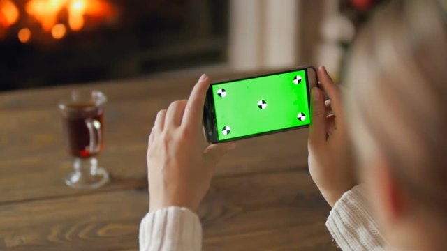Slow motion video of young woman making photos of burning fireplace on smartphone camera. Green chromakey display for inserting your image or video on screen
