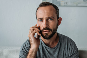 frustrated bearded man talking by smartphone and looking at camera