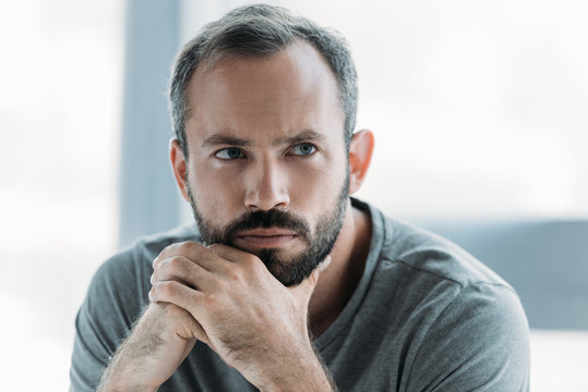 Portrait Of Unhappy Bearded Middle Aged Man With Hands On Chin Looking Away