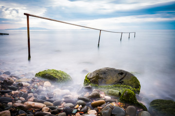 Long exposure of single post standing in flat water and pebble.