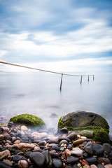 Long exposure of single post standing in flat water and pebble.