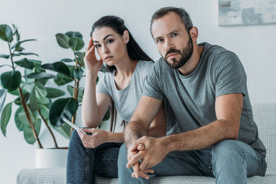 Sad Stressed Couple With Pregnancy Test Sitting And Looking At Camera